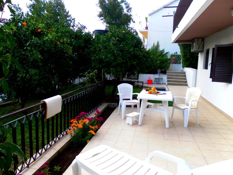 Terrasse des Hauses in Herceg Novi, Montenegro: Kunststoffmöbel, Blick auf den Garten mit Zitrusbäumen und Fliesenboden.