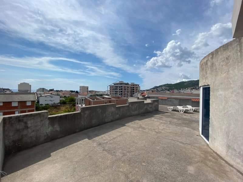 Otvorena terasa s pogledom na grad i planine u kući u Šušnju, Crna Gora, sa ležaljkama i betonskom ogradom.