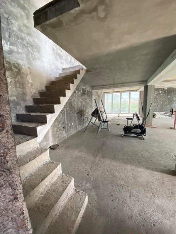 Dvonivo kuća u Šušnju, Crna Gora: betonsko stepenište, gruba završna obrada i sprave za vežbanje u prostranoj prostoriji.