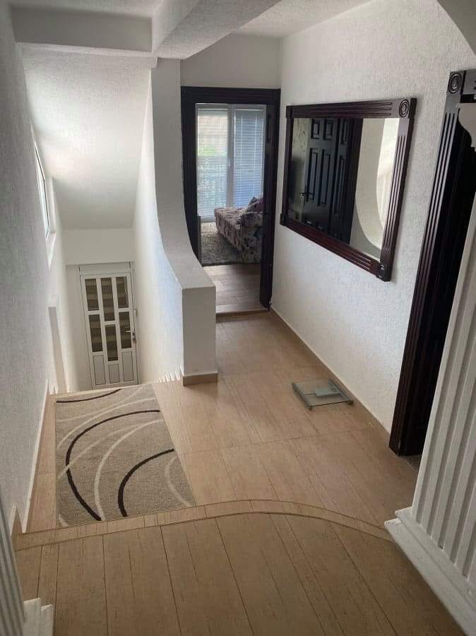 Svetao hodnik sa stepenicama i ogledalom u kući, Šušanj, Crna Gora. Pločice na podu, beli zidovi i pogled na sobu.