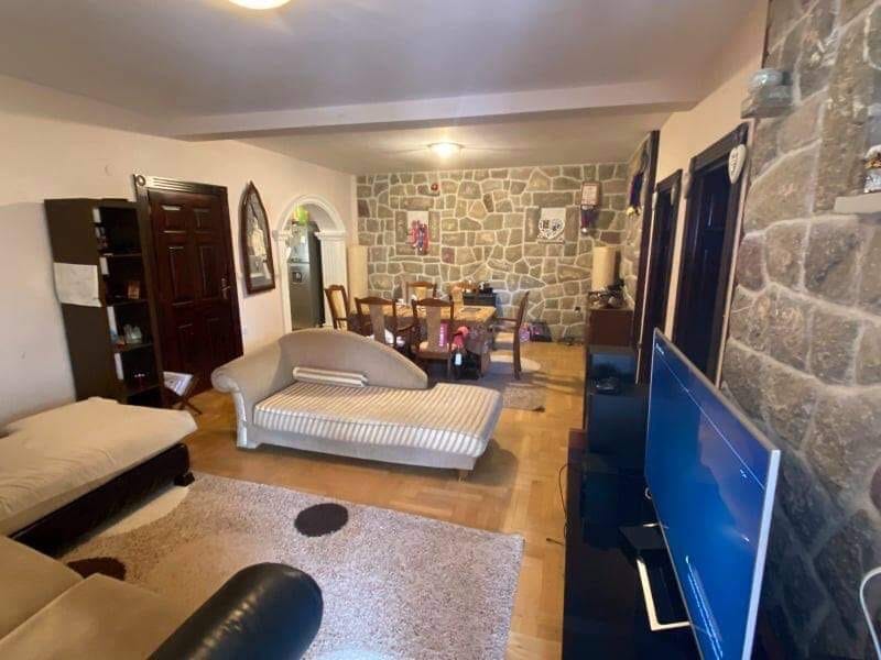 Dnevna soba u kući u Šušnju, Crna Gora: kamena obloga zidova, mekani nameštaj, trpezarijski deo i TV zona.