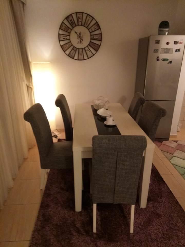 Trpezarijski deo u dnevnoj sobi kuće u Šušnju, Crna Gora: svetli sto, sive stolice, zidni sat i frižider.