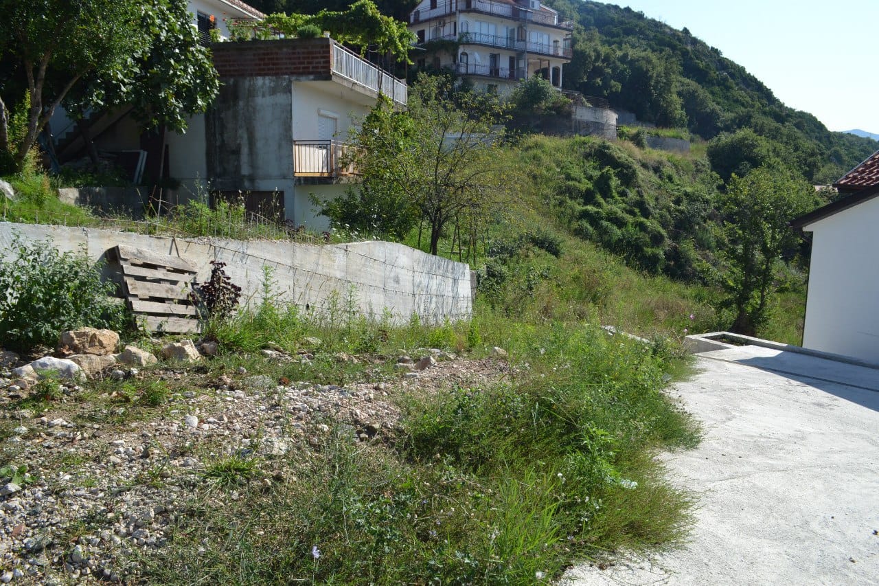 Baugrundstück in Herceg Novi, Montenegro: Blick auf das hügelige Gelände mit Betonzaun und Grünflächen.