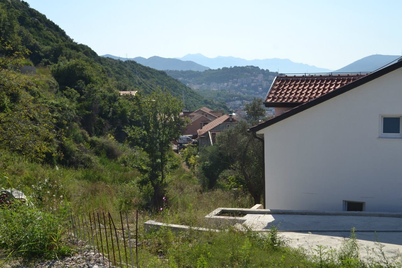 Grundstück in Herceg Novi, Montenegro: Blick auf die Berge, Grünflächen und benachbarte Häuser mit Ziegeldächern.