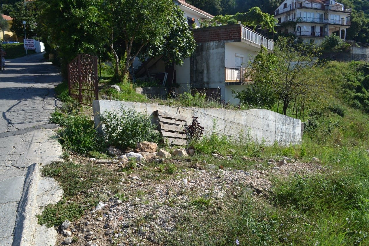 Baugrundstück in Herceg Novi, Montenegro: Blick auf das Grundstück mit Betonumzäunung und Zufahrtsstraße