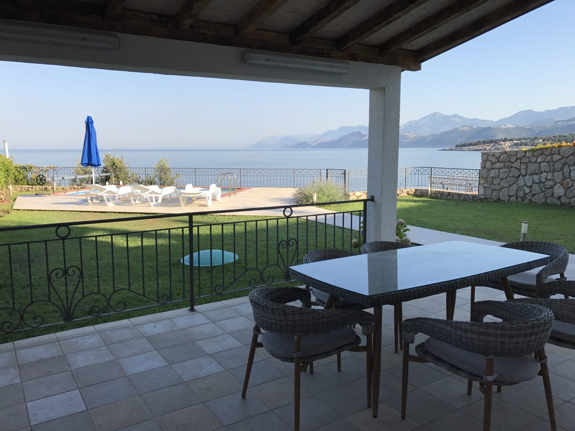 Terrasse de la villa à Utjeha, Monténégro : mobilier en osier, vue sur la mer, piscine et montagnes, revêtement en carrelage et pelouse.