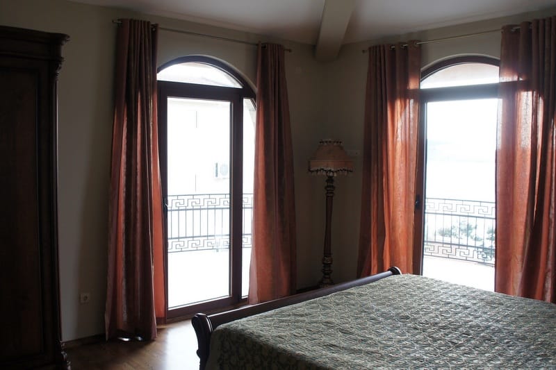 Spavaća soba u kući u Šušnju, Crna Gora: bračni krevet, drveni ormar, podna lampa i izlaz na balkon sa panoramskim prozorima