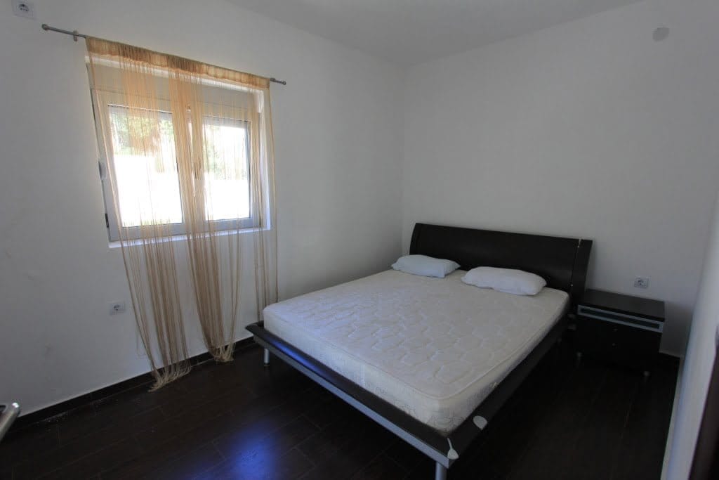 Chambre lumineuse avec lit double et sol sombre dans un mini-hôtel, Orahovac, Monténégro. Vue sur la fenêtre avec voilage.