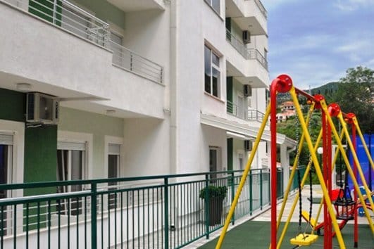 Complexe résidentiel moderne avec aire de jeux pour enfants et terrasses à Herceg Novi, Monténégro. Vue de la façade de l’immeuble.