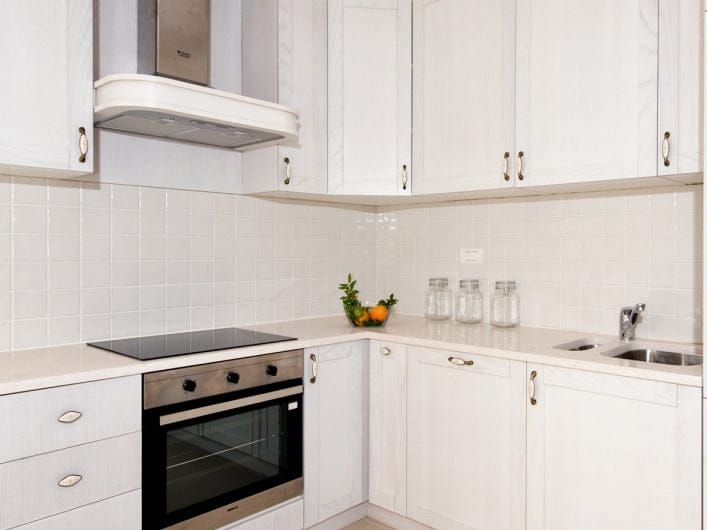 Cuisine lumineuse dans un appartement à Herceg Novi, Monténégro : façades blanches, électroménager encastré, plaque de cuisson et crédence en carrelage.