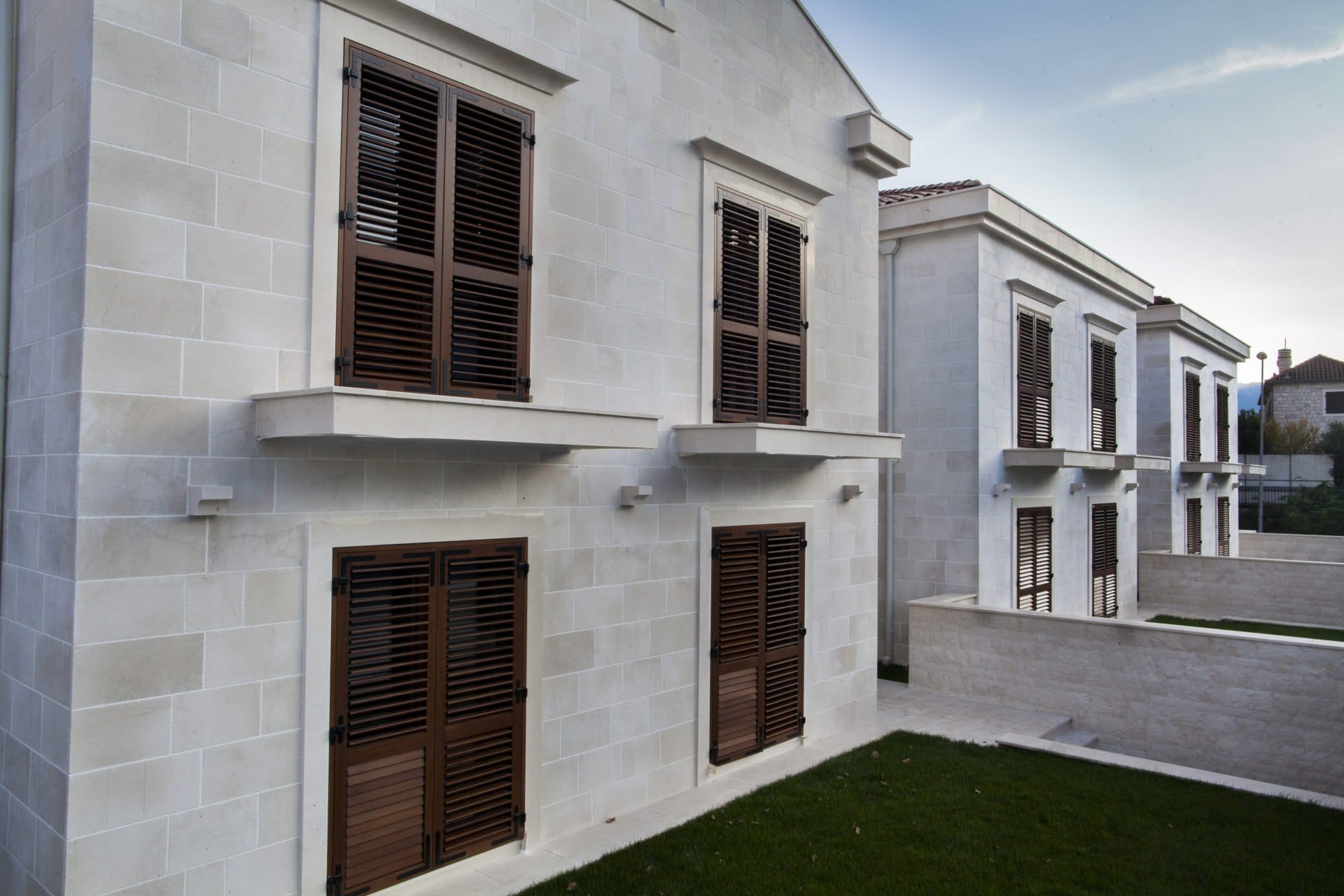 Fassade des Wohnkomplexes in Dobrota, Montenegro: Steinverkleidung der Wände und braune Holzläden an den Fenstern.