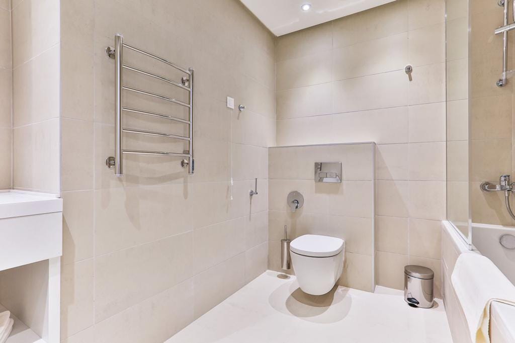 Modern bathroom with beige tiles, wall-mounted toilet, and towel warmer in a residential complex, Rafailovići, Montenegro.
