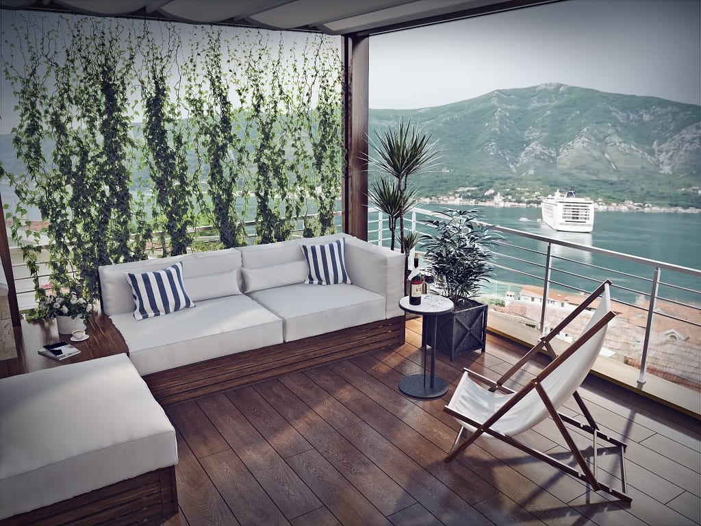 Terrasse der Wohnung in Dobrota, Montenegro: Blick auf die Bucht von Kotor, Holzbelag, weiche Möbel und eine Sonnenliege.