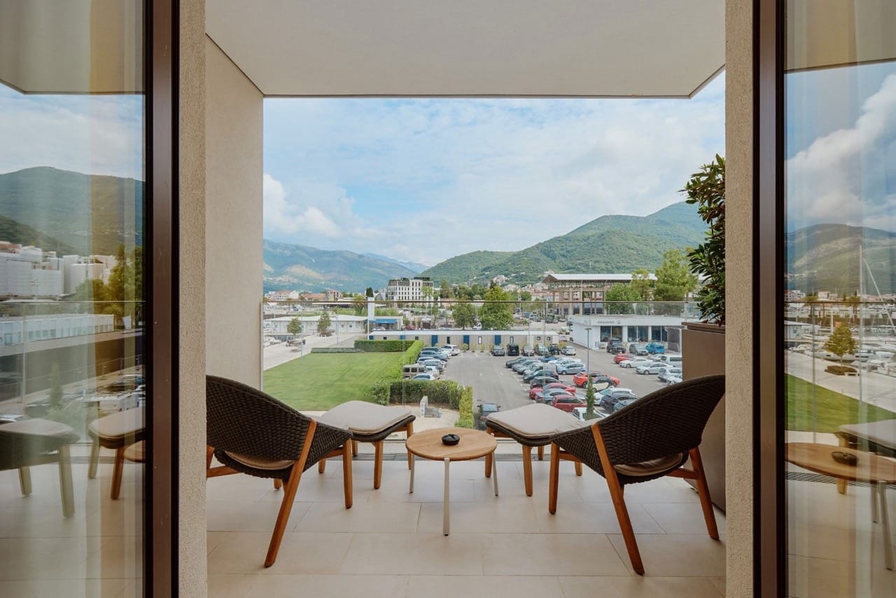 Pogled sa balkona stana u Porto Montenegru, Tivat, Crna Gora: pleteni nameštaj i panoramski pogled na planine i marinu.