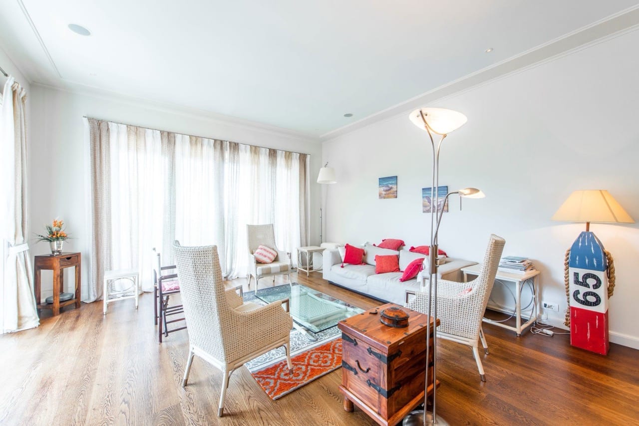 Svetla dnevna soba u stanu Porto Montenegro, Tivat, Crna Gora: pletene fotelje, sofa sa crvenim jastucima, dekor.