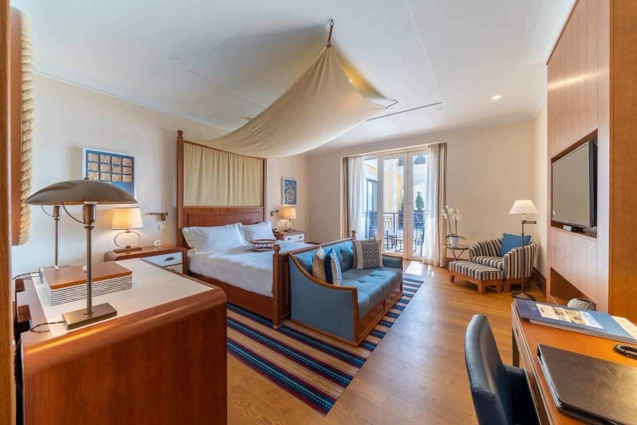 Enterijer spavaće sobe u apartmanima Porto Montenegro, Tivat, Crna Gora: krevet s baldahinom, plava sofa i pogled na terasu.
