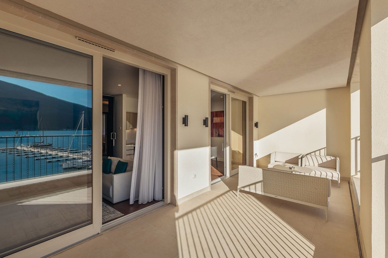 Terrasse spacieuse avec mobilier en osier dans l’appartement Portonovi, Kumbor, Monténégro, avec vue sur la marina de yachts et la mer.