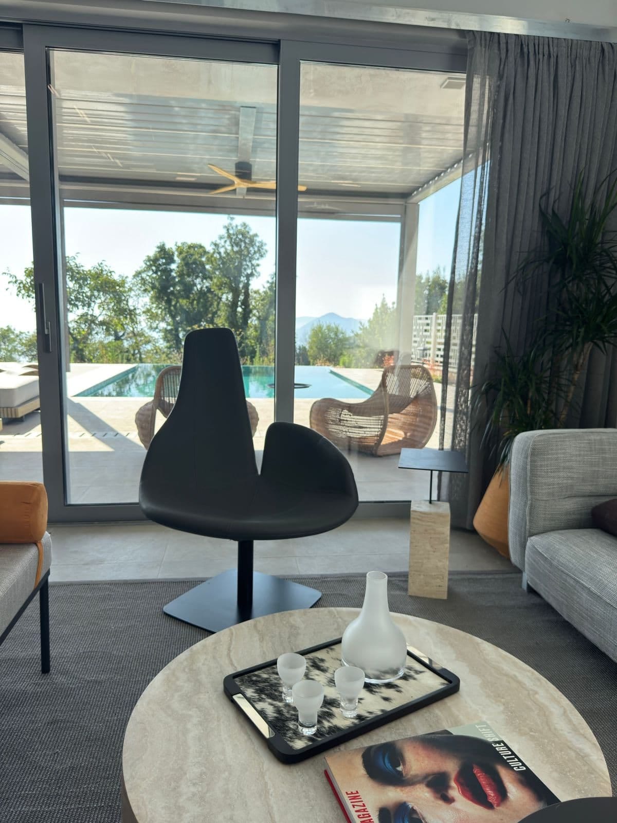 Salon willi w Blizikuće, Czarnogóra: panoramiczne okna, widok na basen, designerski fotel i marmurowy stolik.