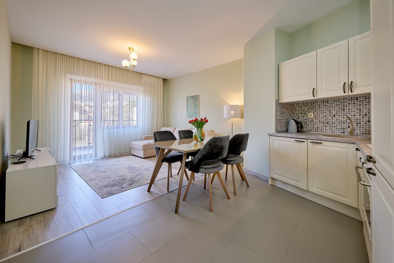 Salon moderne avec cuisine dans un appartement, Rafailovici, Monténégro : intérieur lumineux, coin repas et accès au balcon.