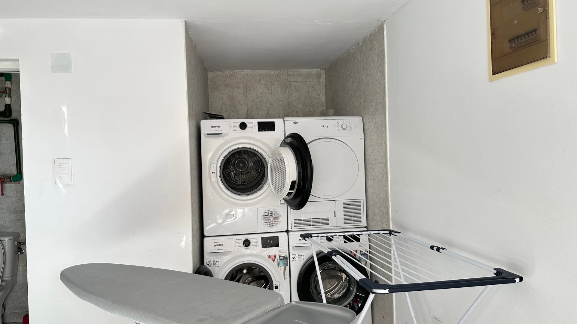 Laundry area in a hotel in Pržno, Montenegro: washing and drying machines, ironing board, and clothes drying rack.