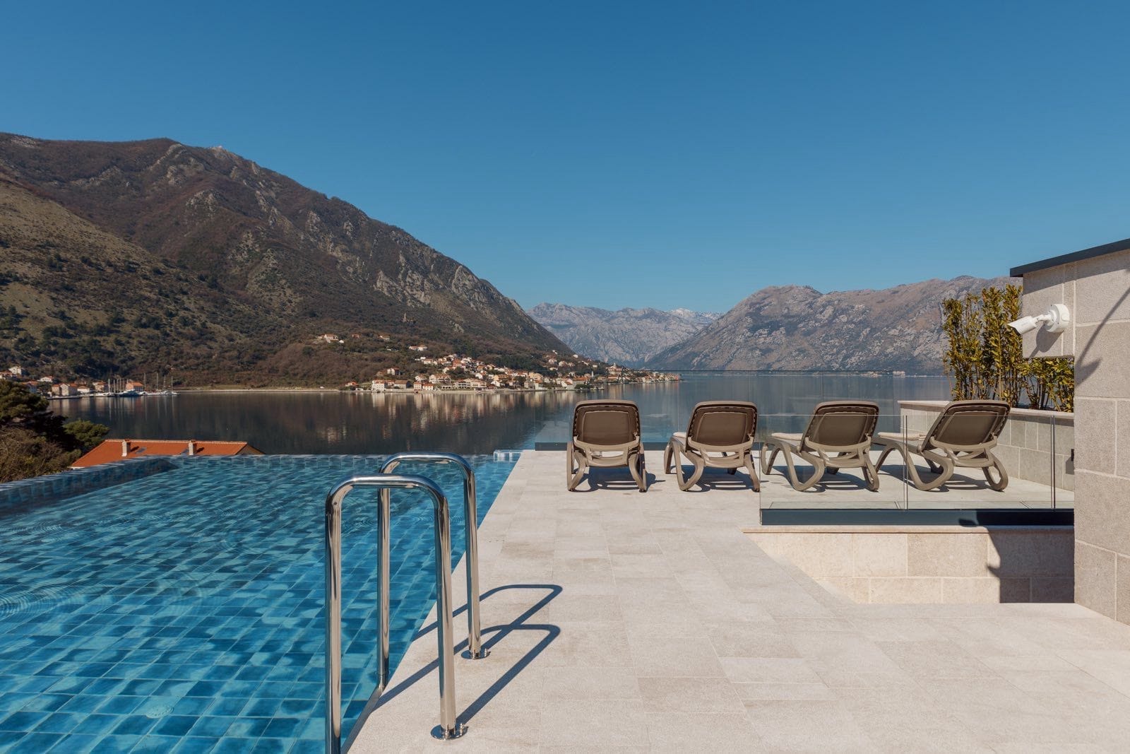 Infinity pool with views of Kotor Bay and the mountains in Dobrota, Montenegro, terrace with sun loungers by apartment No. 2412.