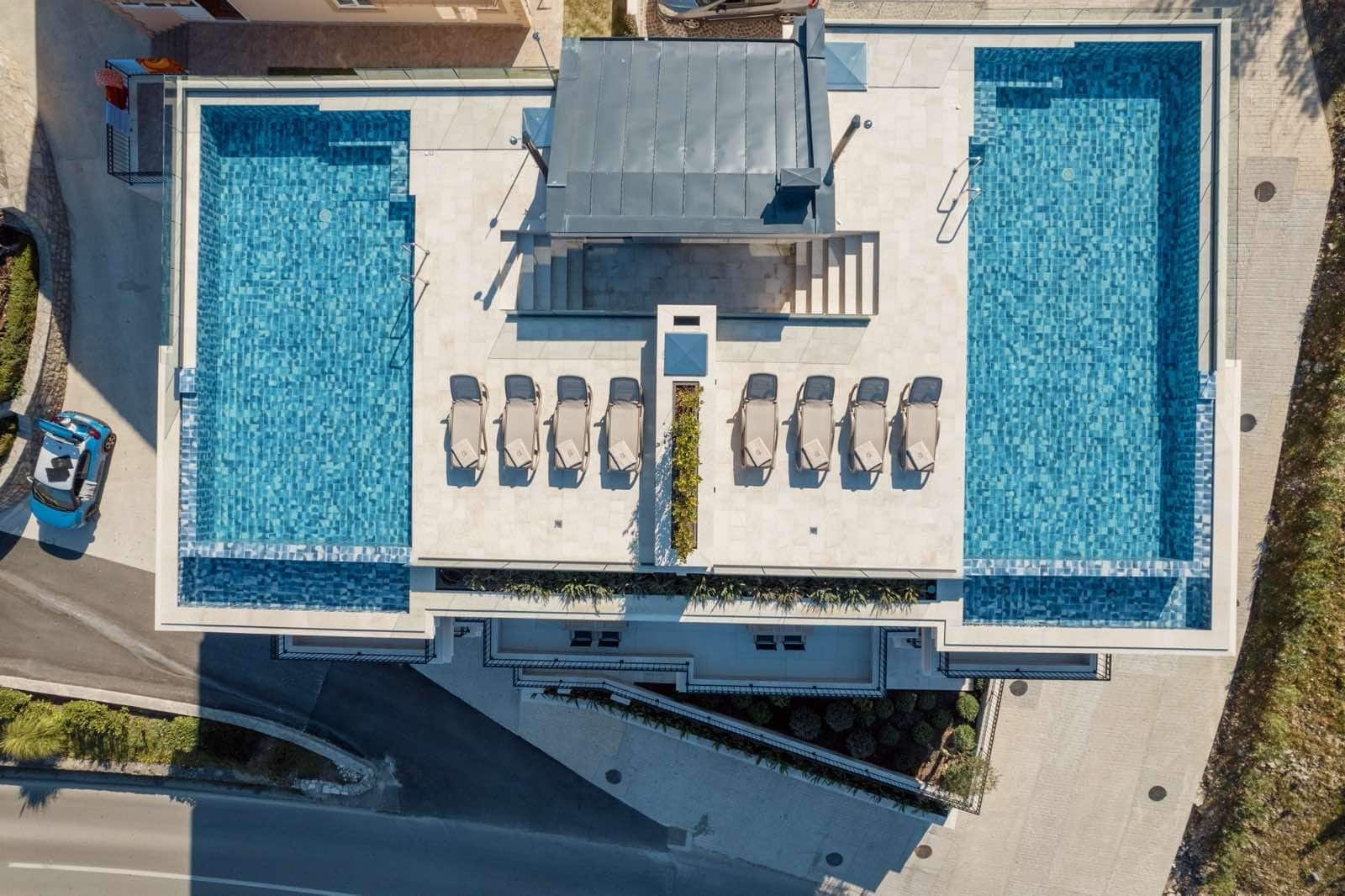 Draufsicht auf eine Terrasse mit zwei Pools und Sonnenliegen in einem Apartment in Dobrota, Montenegro.