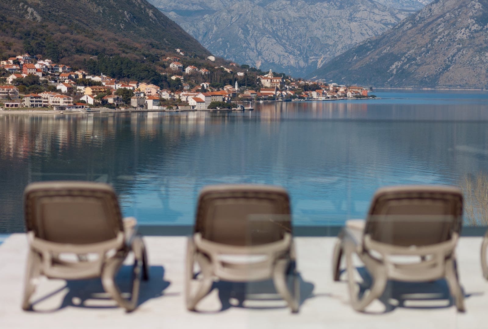 Sun loungers by the pool with panoramic views of Kotor Bay and the town of Dobrota, Montenegro.