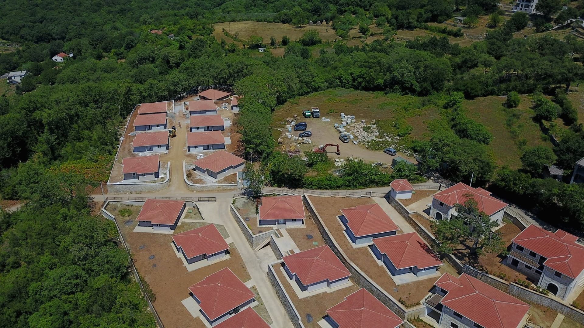 Aerial view of a cottage community under construction with tiled roofs surrounded by forest, Bar, Montenegro.