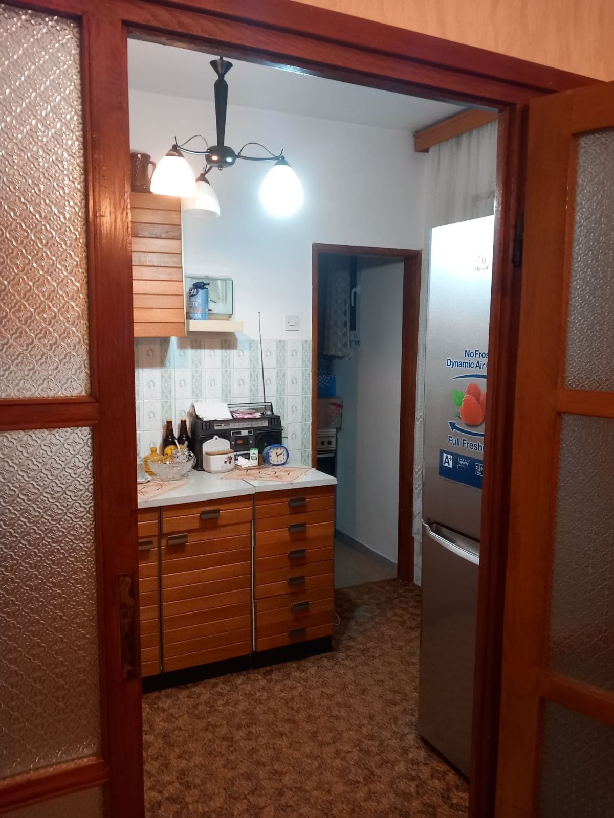 Кухня с деревянными фасадами и холодильником в доме на продажу в Игало, Черногория. Вид через дверной проем.