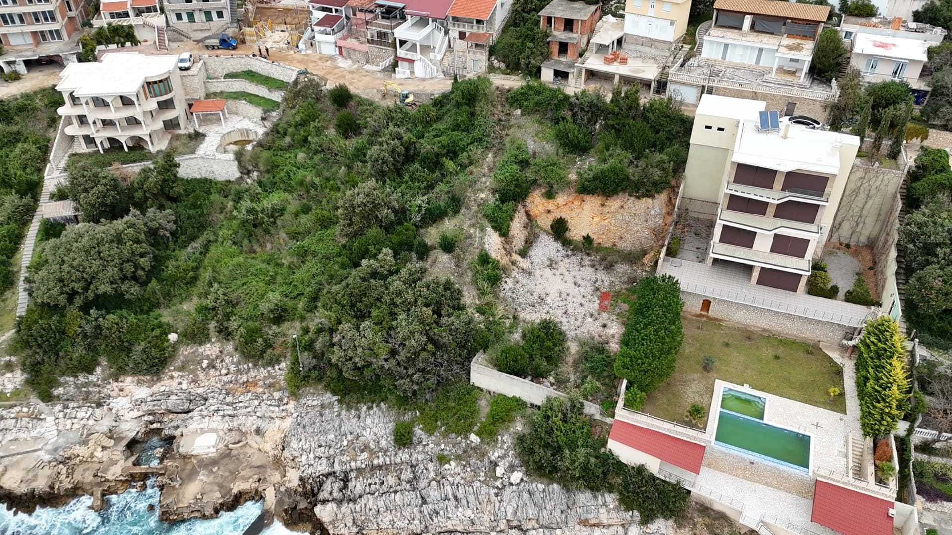 Building plot by the sea in Montenegro with a view of the coastline, swimming pool, and neighboring villas, aerial view.