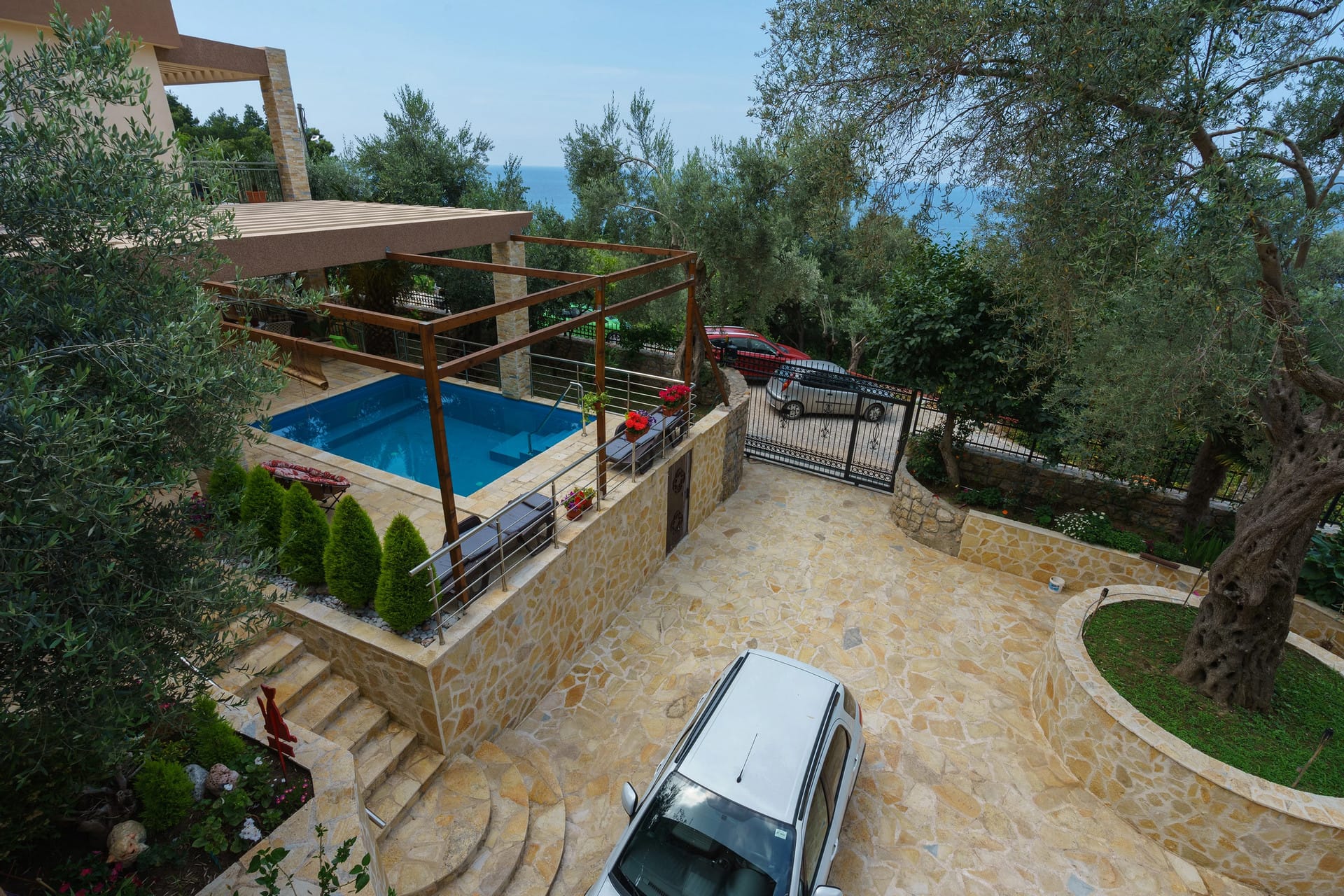 Sutomore, Karadağ'da ev bahçesi: teraslı yüzme havuzu, taş kaplama, otopark ve zeytin ağaçları arasında deniz manzarası.