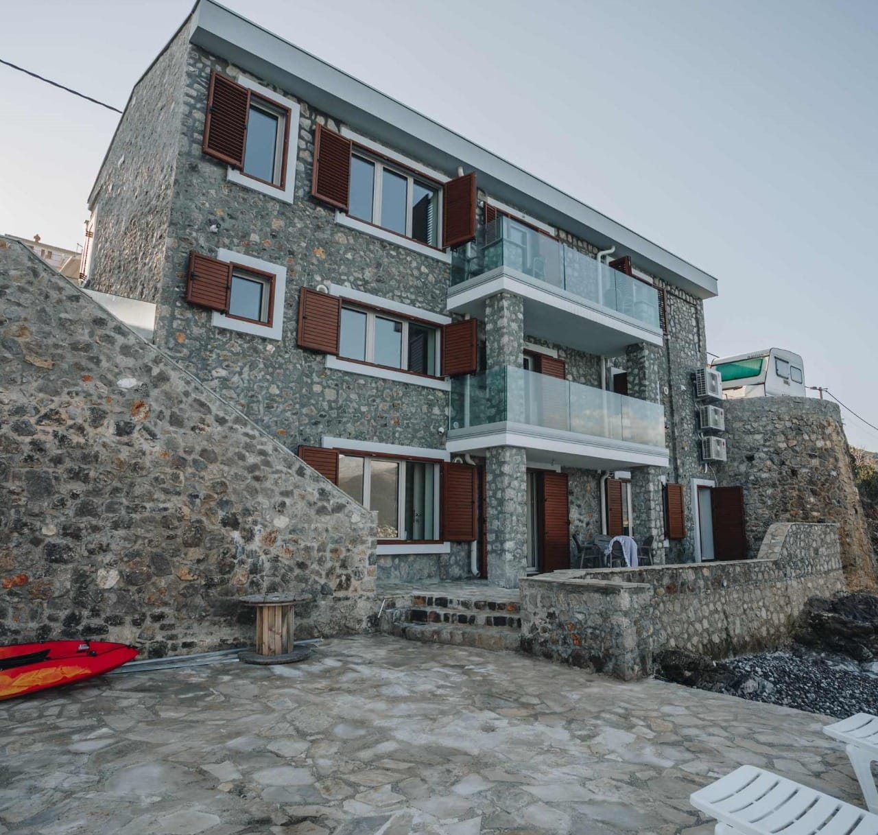 Трехэтажная каменная вилла в Крашичи, Черногория, с террасами, стеклянными ограждениями и видом на море.