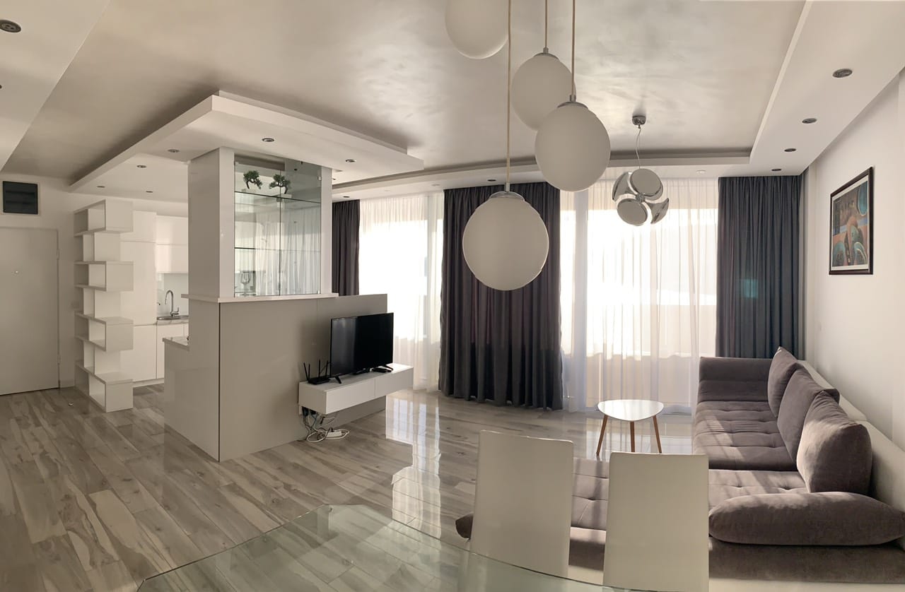 Modernes Wohnzimmer mit Küche in einem Apartment, Rafailovići, Montenegro: graues Sofa, Designerleuchten und helles Interieur.