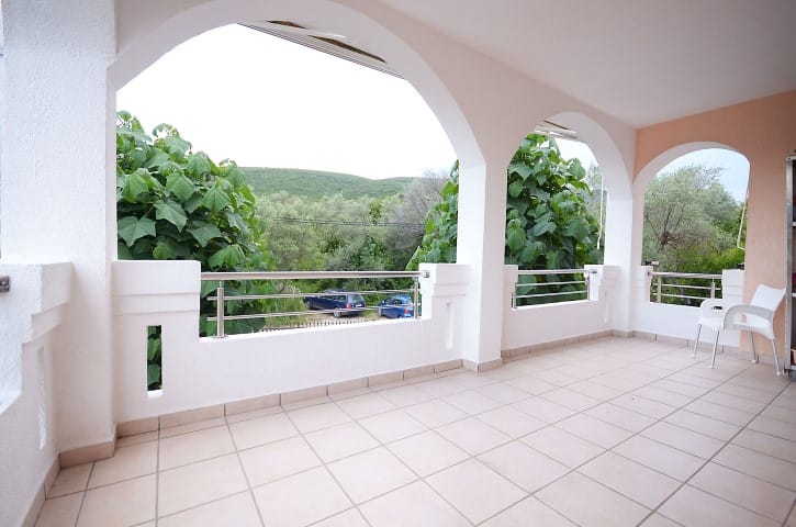 Geräumige Terrasse mit Rundbögen und Blick ins Grüne in einem Haus in Krašići, Montenegro. Fliesenboden, weiße Geländer.