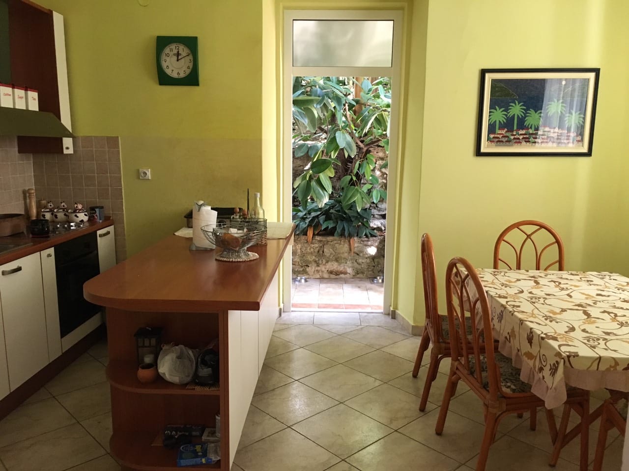 Kuhinja sa šankom i trpezarijom u kući u Herceg Novom, Crna Gora, sa izlazom u zelenu baštu kroz staklena vrata.