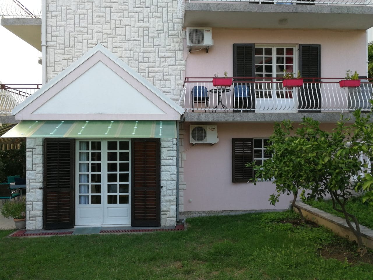 Fasada kuće u Tivtu, Crna Gora: terasa sa nameštajem, kamena obloga, balkon i zelena bašta kod ulaza.