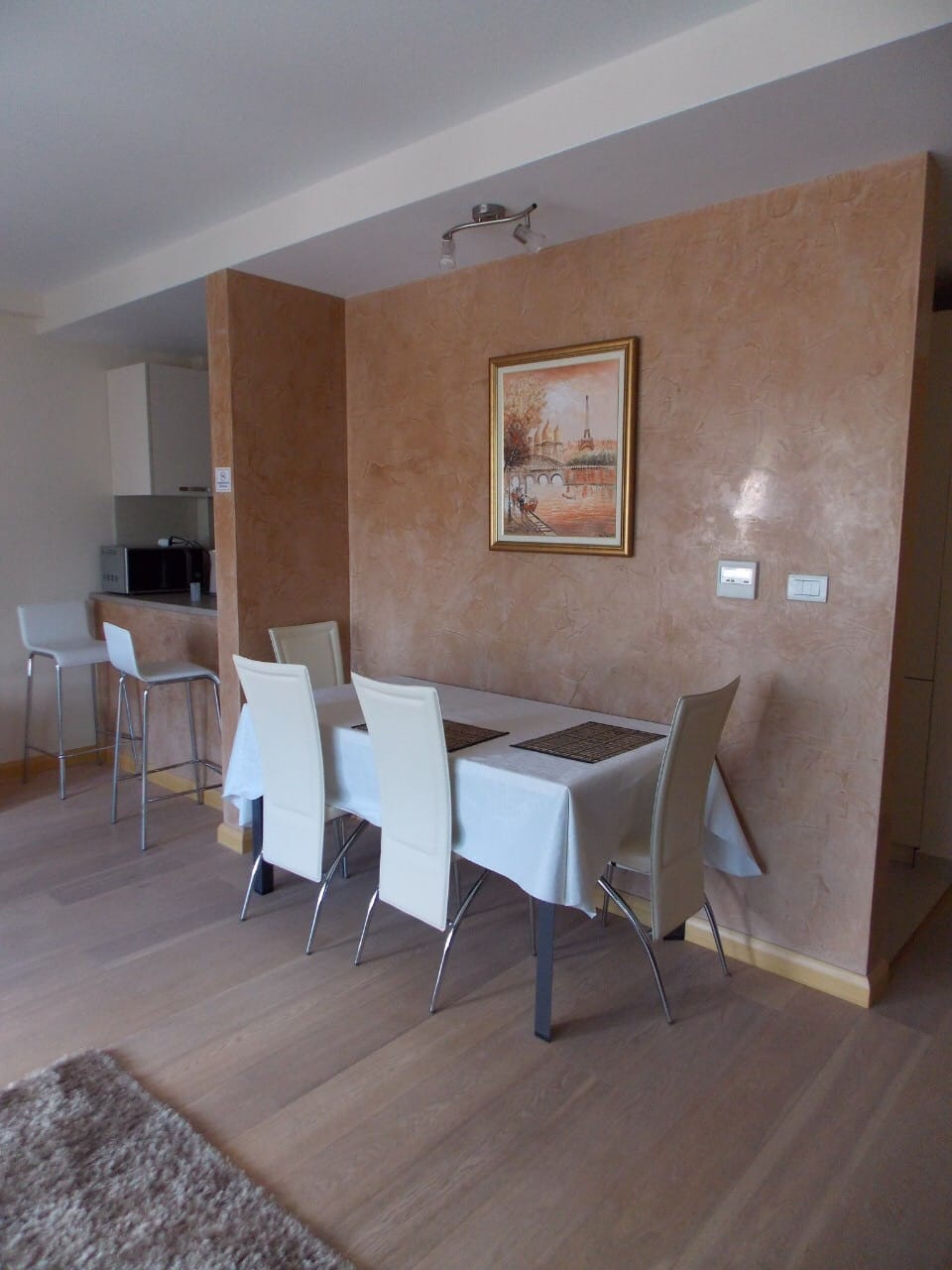 Обеденная зона в квартире в Будве, Черногория: светлая мебель, декоративная штукатурка стен и барная стойка на кухне.