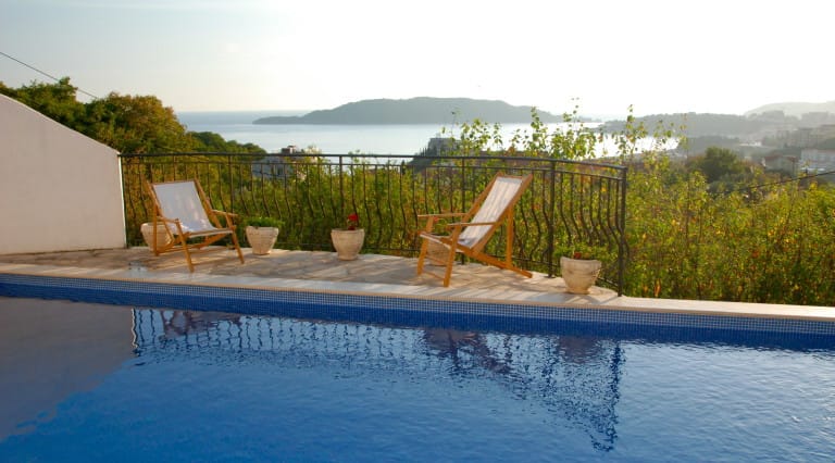 Terrasse avec piscine et chaises longues dans une villa à Bečići, au Monténégro, offrant une vue panoramique sur la mer et l'île de Sveti Stefan.