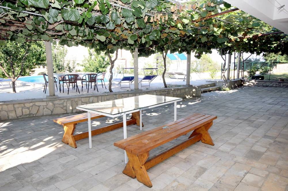 Terasa kuće u Reževićima, Crna Gora: kameni pod, drvene klupe, nadstrešnica od vinove loze i pogled na bazen.