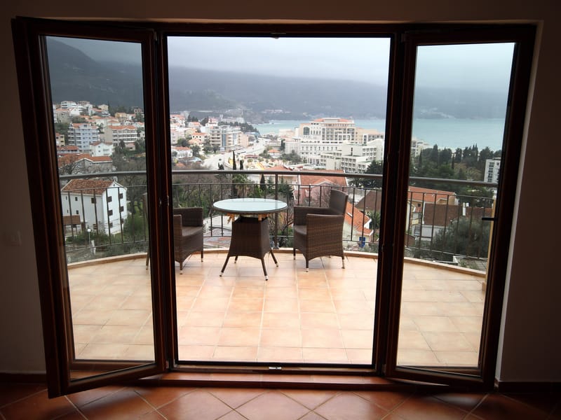 Beçiçi, Karadağ'daki dairenin terasından manzara: hasır mobilyalar, panoramik deniz, dağ ve tatil köyü otelleri manzarası.