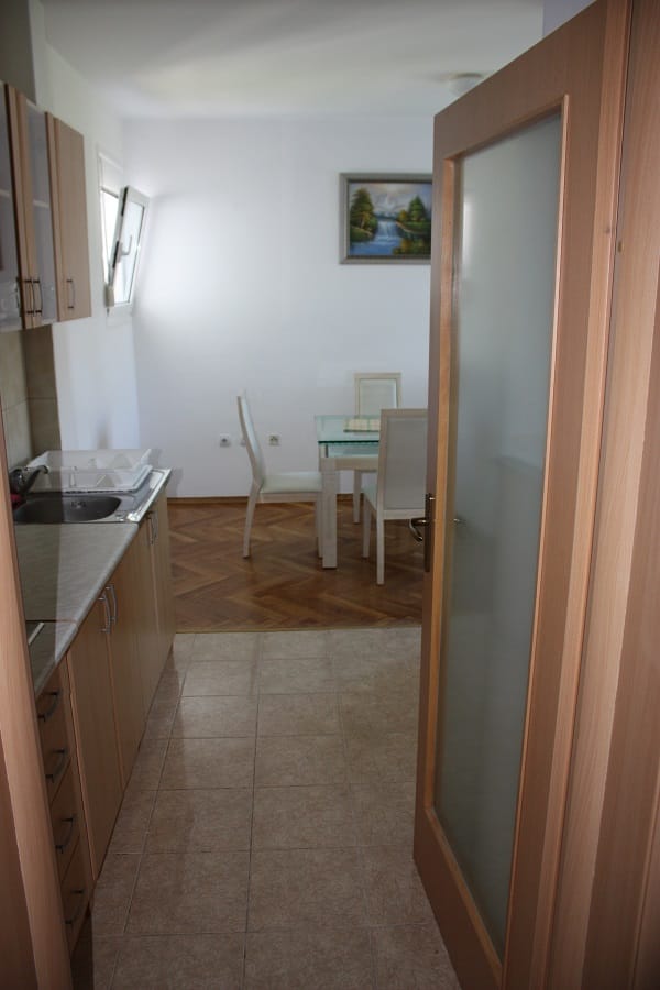 Kuhinja sa drvenim nameštajem i trpezarijski deo u stanu u Budvi, Crna Gora: pločice na podu i parket u dnevnoj sobi.