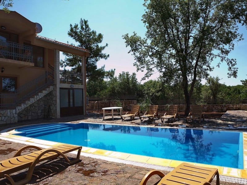 Dvospratna kuća sa bazenom i prostorom za odmor u Krimovici, Crna Gora: ležaljke, terasa i kamena fasada.