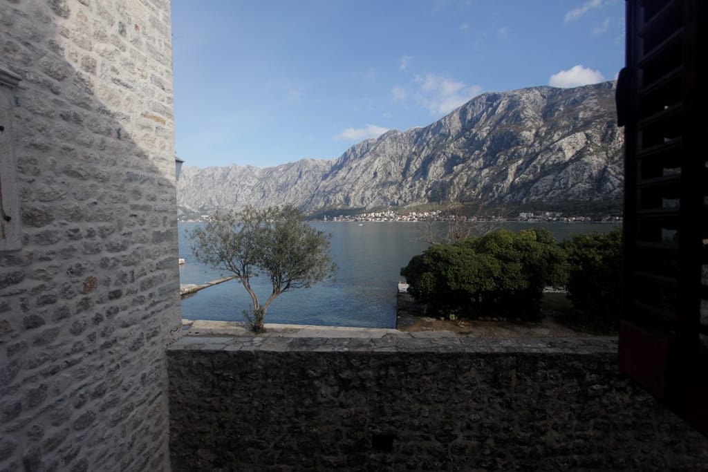 Вид на Которский залив и горы из каменного дома в Прчани, Черногория: терраса с каменной кладкой и панорамный морской пейзаж.