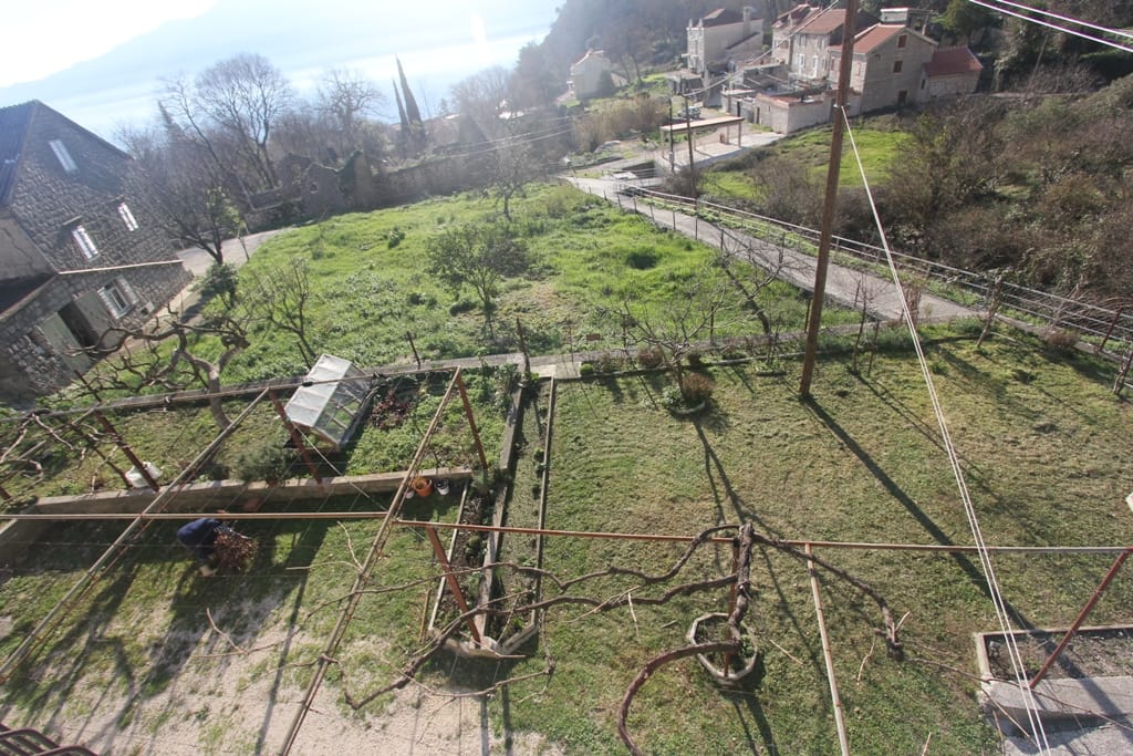 View of a green plot with a vineyard and a stone house in Orahovac, Montenegro, with panoramic sea and mountain views.