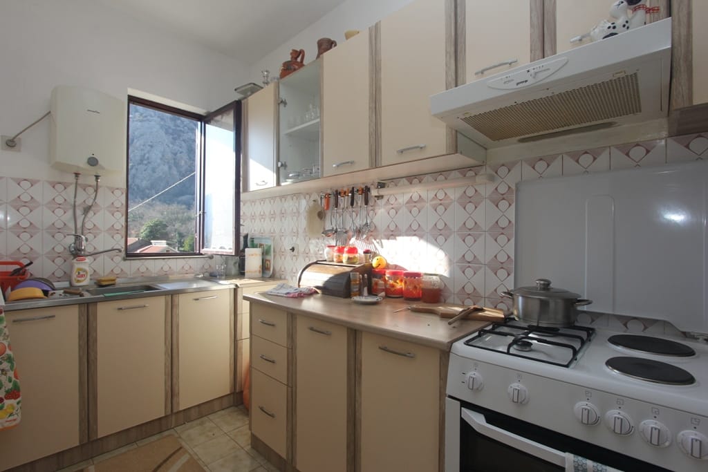 Bright kitchen in a house in Orahovac, Montenegro: beige cabinets, gas stove, and mountain view from the window.