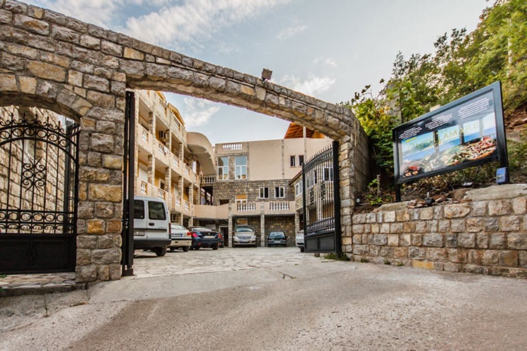 Въезд в отель Castellamare с каменной аркой и парковкой, Булярица, Черногория: вид на фасад здания снаружи.