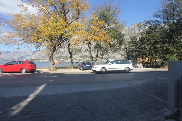 Вид на Которский залив и горы из дома в Муо, Черногория: дорога, припаркованные автомобили и осенние деревья.