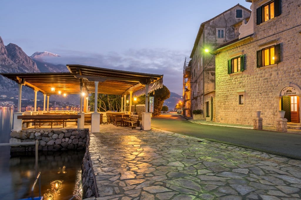 Вечерняя набережная с каменной террасой у моря и старинная вилла в Прчани, Черногория, вид на горы и залив.