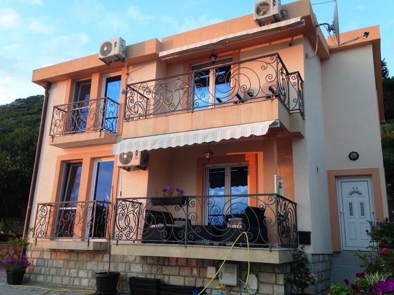 Two-story house with wrought-iron balconies and a terrace in Dobri Vody, Montenegro: facade with stone cladding and air conditioners.