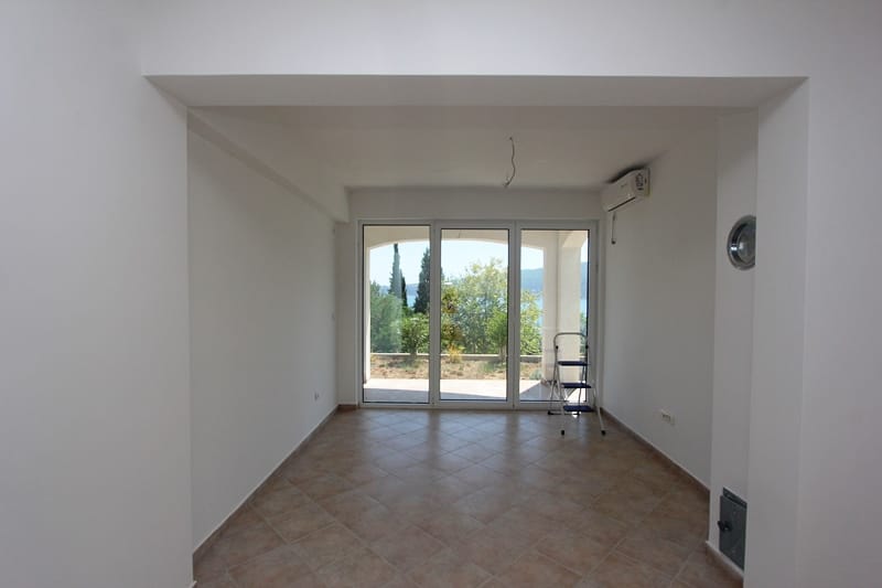 Bright living room with panoramic windows and sea view in a house, Baošići, Montenegro. Tiled floor and white walls.
